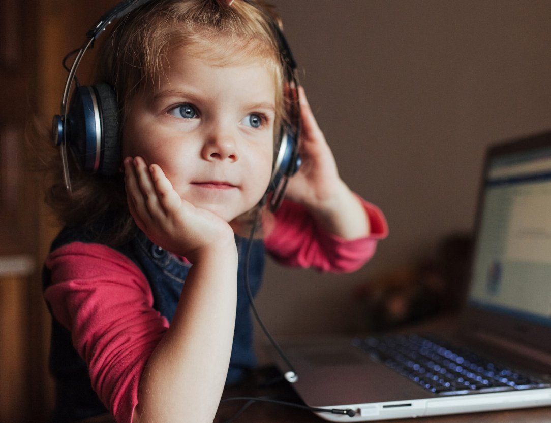 little girl with headphones listening to music, using laptop.